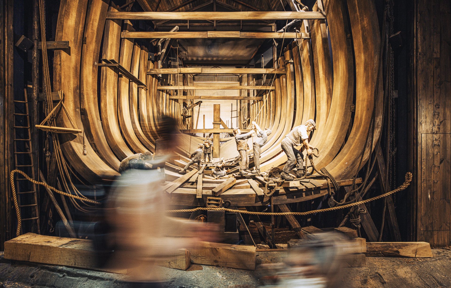 A visitor walks by a diorama of the inside of the RRS Discovery during its construction in the Dundee dockyards. A golden glow radiates from behind the ship's structure.